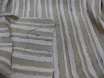 Tissu en lin rayé beige et blanc, couture centrale avec fils lâches – texture naturelle et détails du tissage visibles