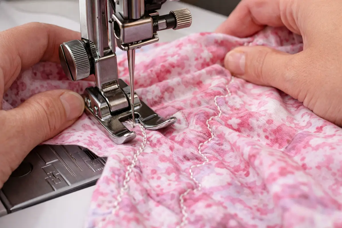 Mains qui poussent et tirent un tissu sous le pied-de-biche d’une machine à coudre provoquant une couture irrégulière